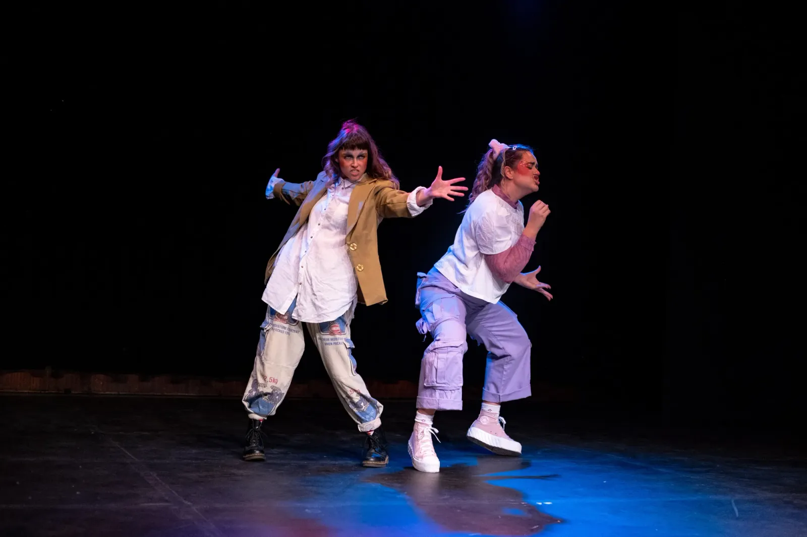 Two people on a darkened stage doing performative movements. 